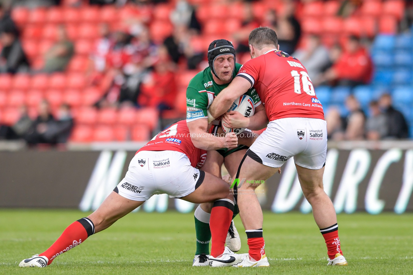 Chris Hill (8) of Warrington Wolves is tackled by Greg Burke (16) of Salford Red Devils and Elijah Taylor (13) of Salford Red Devils
