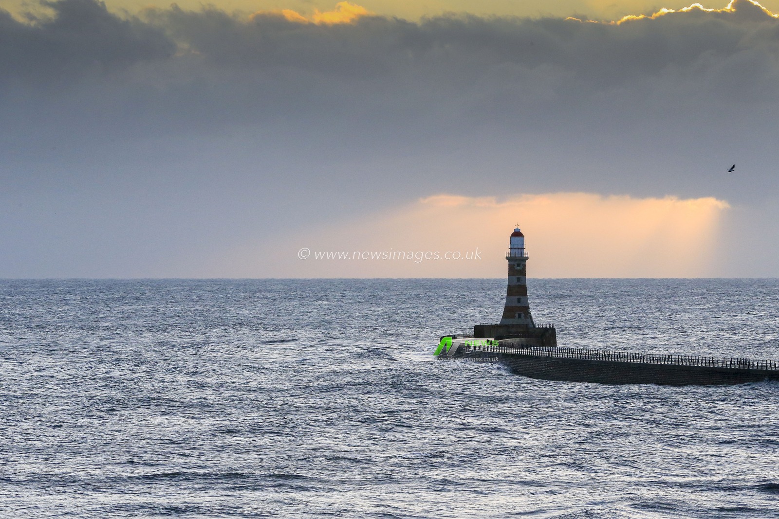 Rays of sun shine through the dark clouds and illuminate Roker Pier and Lighthouse as dawn breaks in Sunderland
