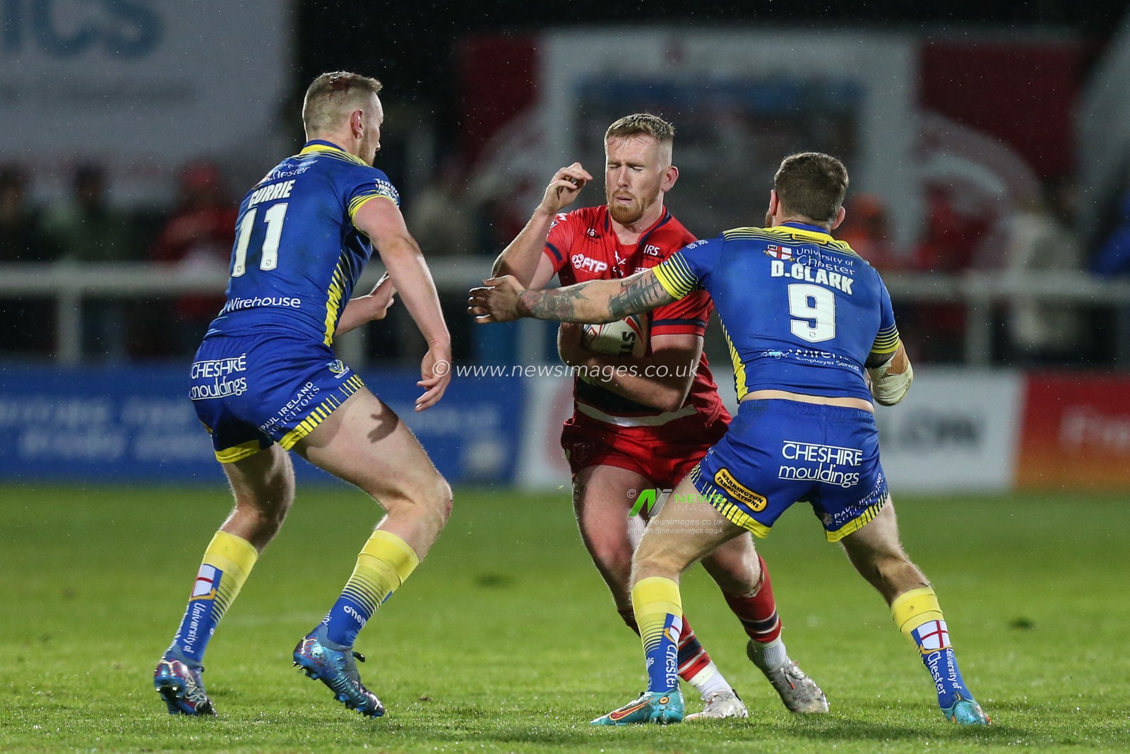 Rowan Milnes #21 of Hull KR runs at Ben Currie #11 and Daryl Clark #9 of Warrington Wolves
