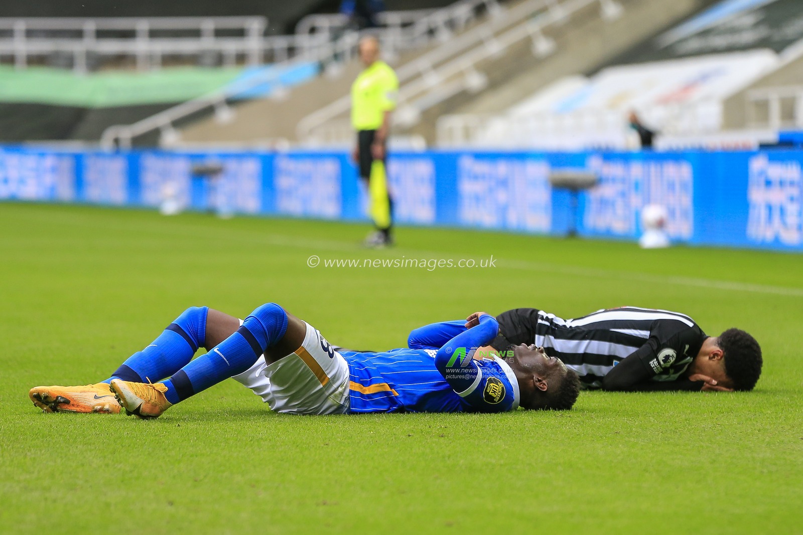 Jamal Lewis (15) of Newcastle United lays on the pitch holding his face as Yves Bissouma (8) of Brighton and Hove Albion lies on his back next to him after the two clashed during a challenge