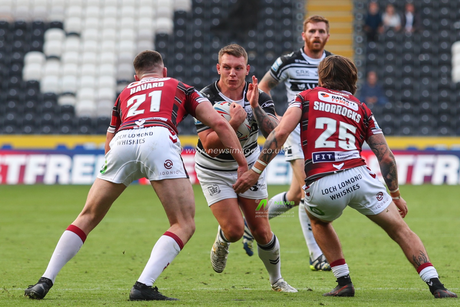 Jordan Lane (16) of Hull FC runs at Ethan Havard (21) and Joe Shorrocks (25) of Wigan Warriors