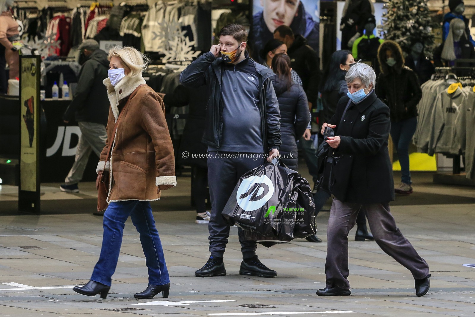 A Christmas shopper stands outside JD Sports, Northumberland Street, Newcastle upon Tyne, with several shopping bags from JD Sports after the end of the country's second national lockdown