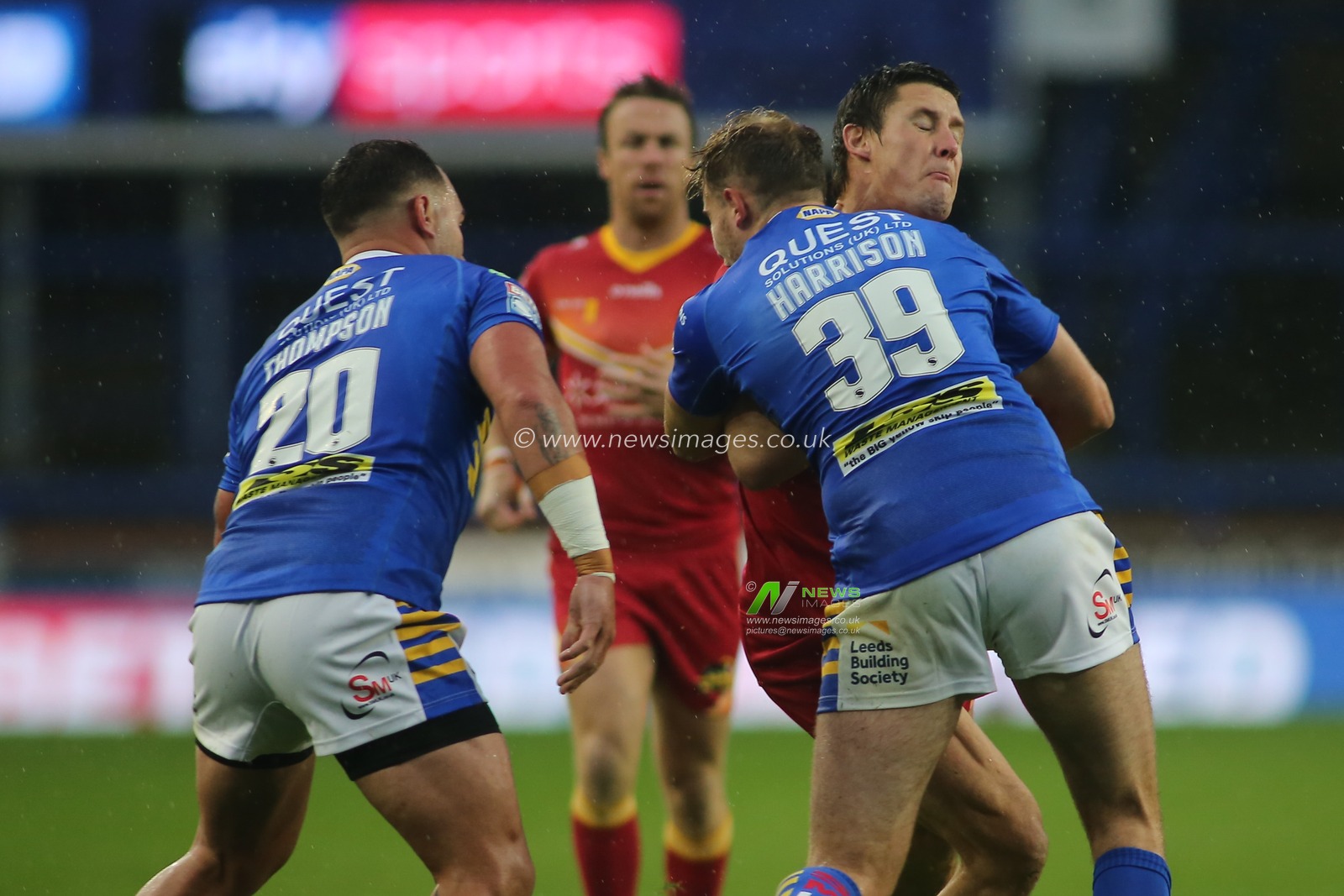 Joel Tomkins(12) of Catalan Dragons tackled by Bodene Thompson (20) and James Harrison of Leeds Rhinos.