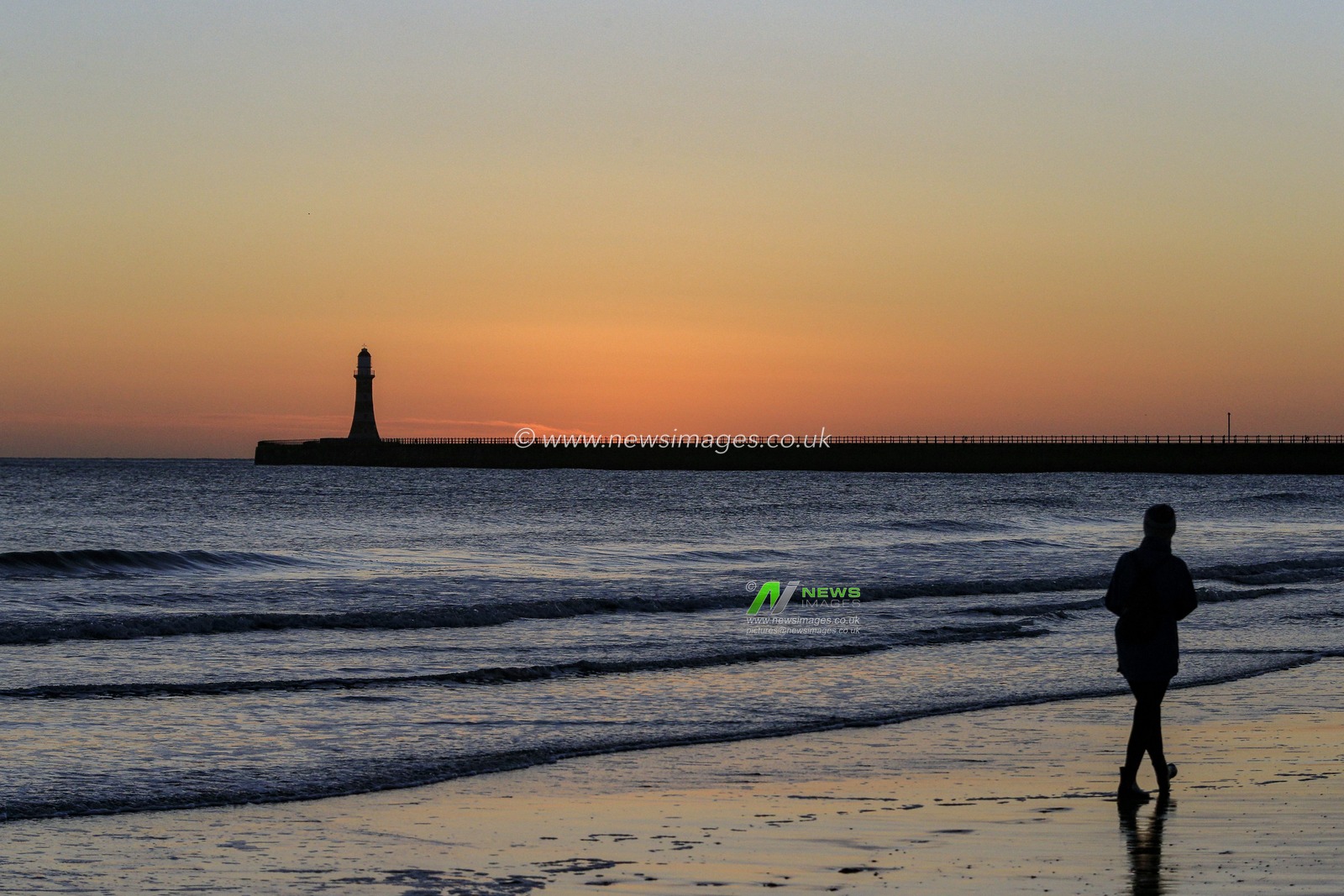 A woman walks along Roker Beach, near Roker Pier and Lighthouse in Sunderland, just before sunrise