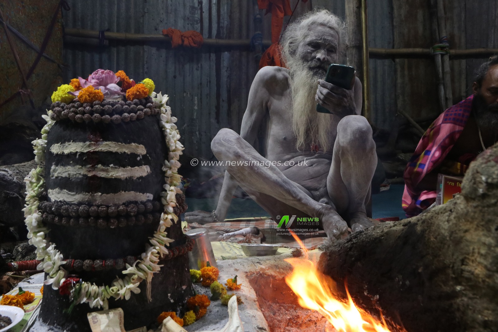 A Naga saint watching news his smartphone  at a transit camp of the Gangasagar fair in Kolkata, India, on January 5, 2025. The Gangasagar Mela is an annual Hindu festival held at Gangasagar, West Bengal, where the Ganges River meets the Bay of Bengal. The fair takes place at Kapilmuni's ashram on Gangasagar every year on Makar Sankranti.Pictures by Debajyoti Chakraborty.(Photo: Debajyoti Chakraborty/News Images)