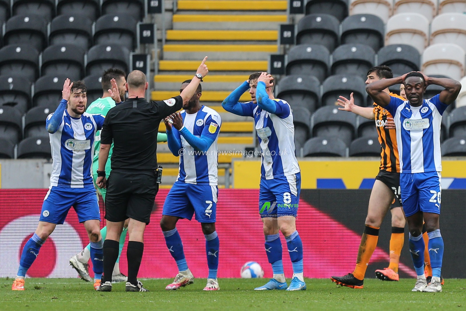 Wigan Athletic players surround referee Robert Madley to appeal for a penalty kick