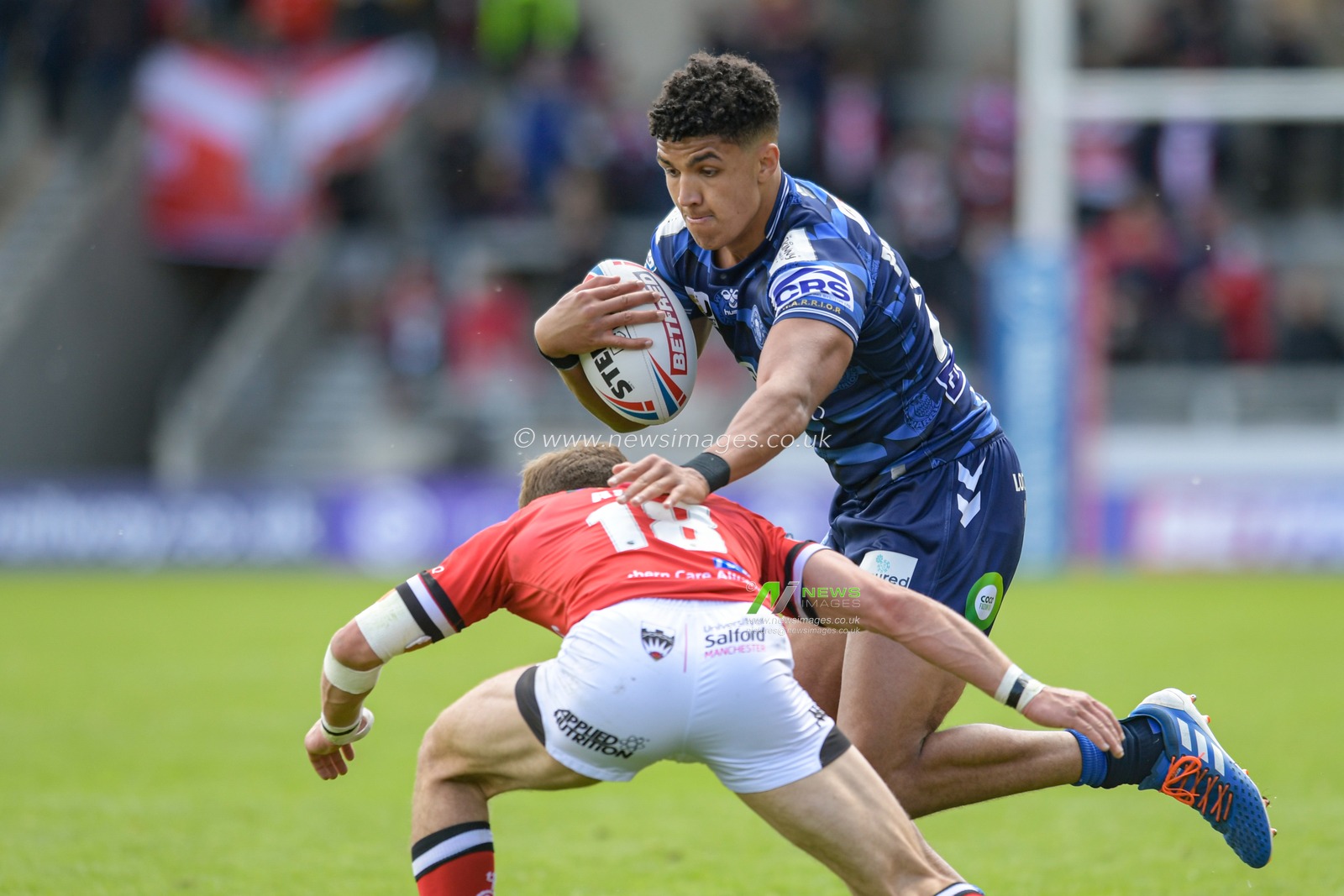 Kai Pearce-Paul (27) of Wigan Warriors is tackled by Chris Atkin (18) of Salford Red Devils