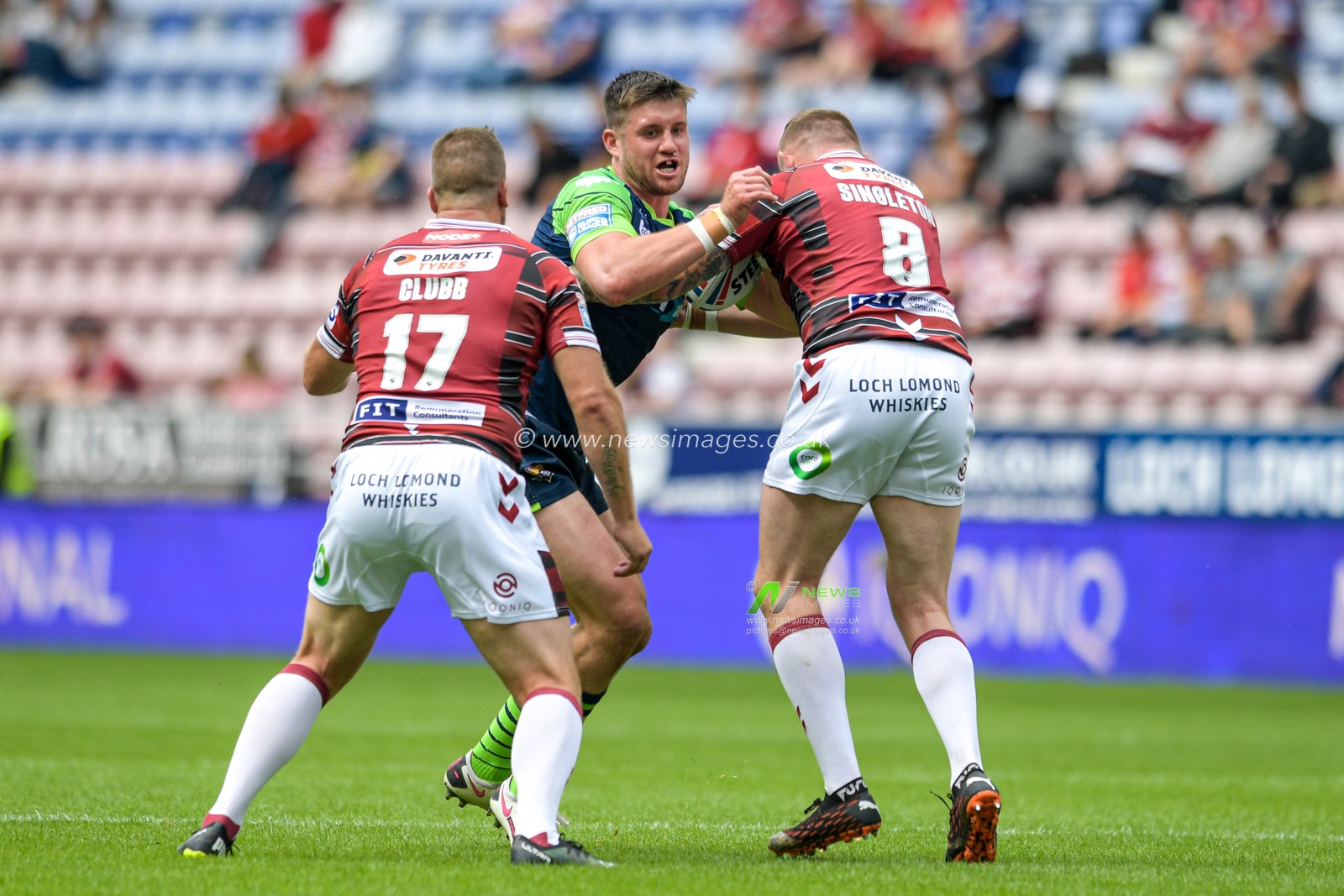 Joe Greenwood (15) of Huddersfield Giants is tackled by Brad Singleton (8) of Wigan Warriors and Tony Clubb (17) of Wigan Warriors