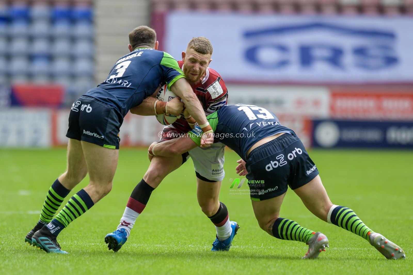 Jackson Hastings (31) of Wigan Warriors is tackled by Josh Jones (13) of Huddersfield Giants and Jake Wardle (3) of Huddersfield Giants