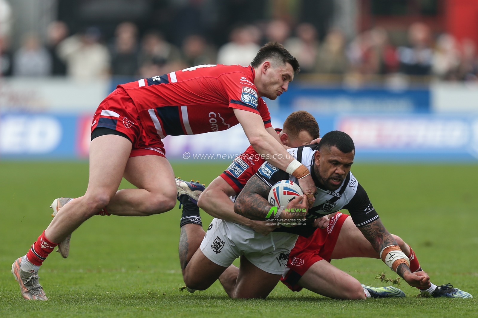 Manu Ma'u #12 of Hull FC is stopped by Frankie Halton #27 and Sam Wood #24 of Hull KR