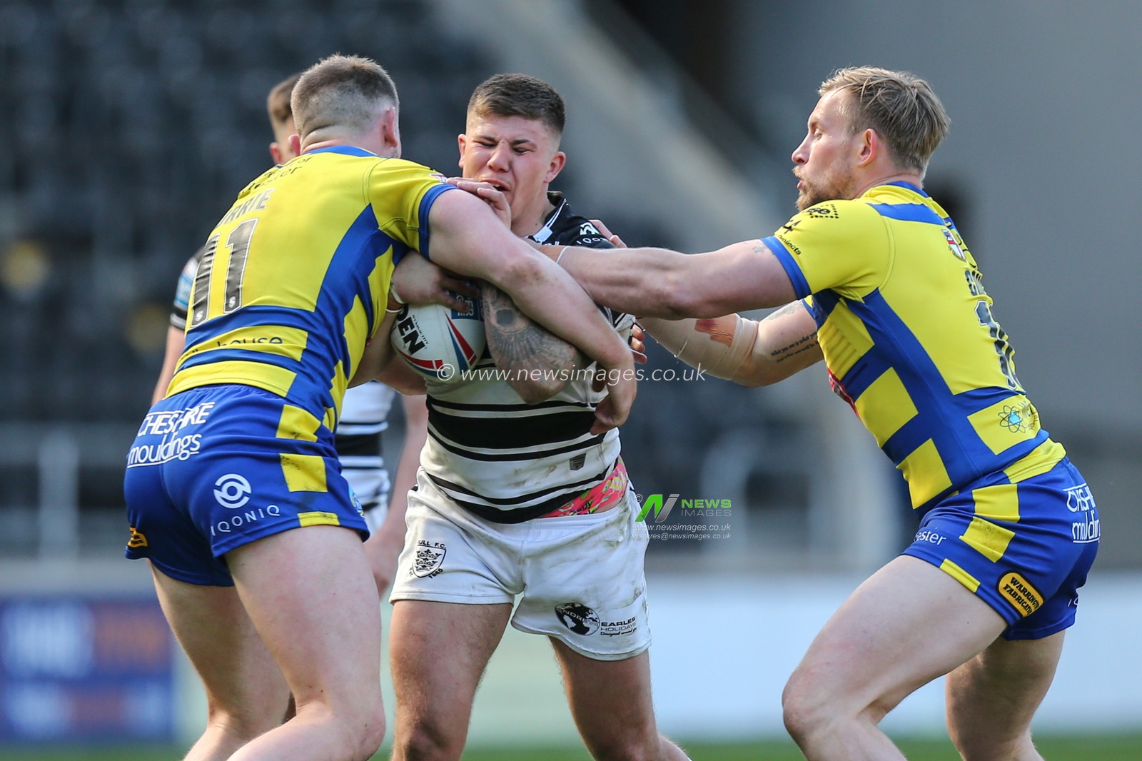 Joe Cator (15) of Hull FC is tackled by Ben Currie (11)  and Mike Cooper (10) of Warrington Wolves