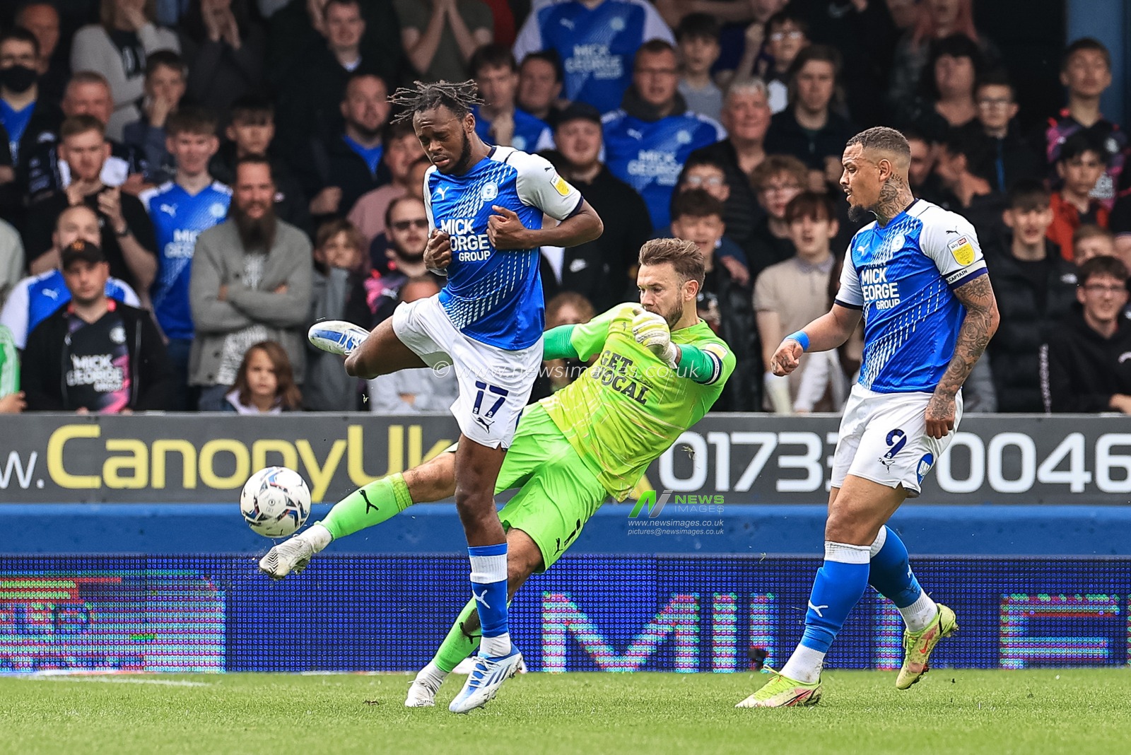 Chris Maxwell #1 of Blackpool clears the ball under pressure from Ricky Jade-Jones #17 of Peterborough United
