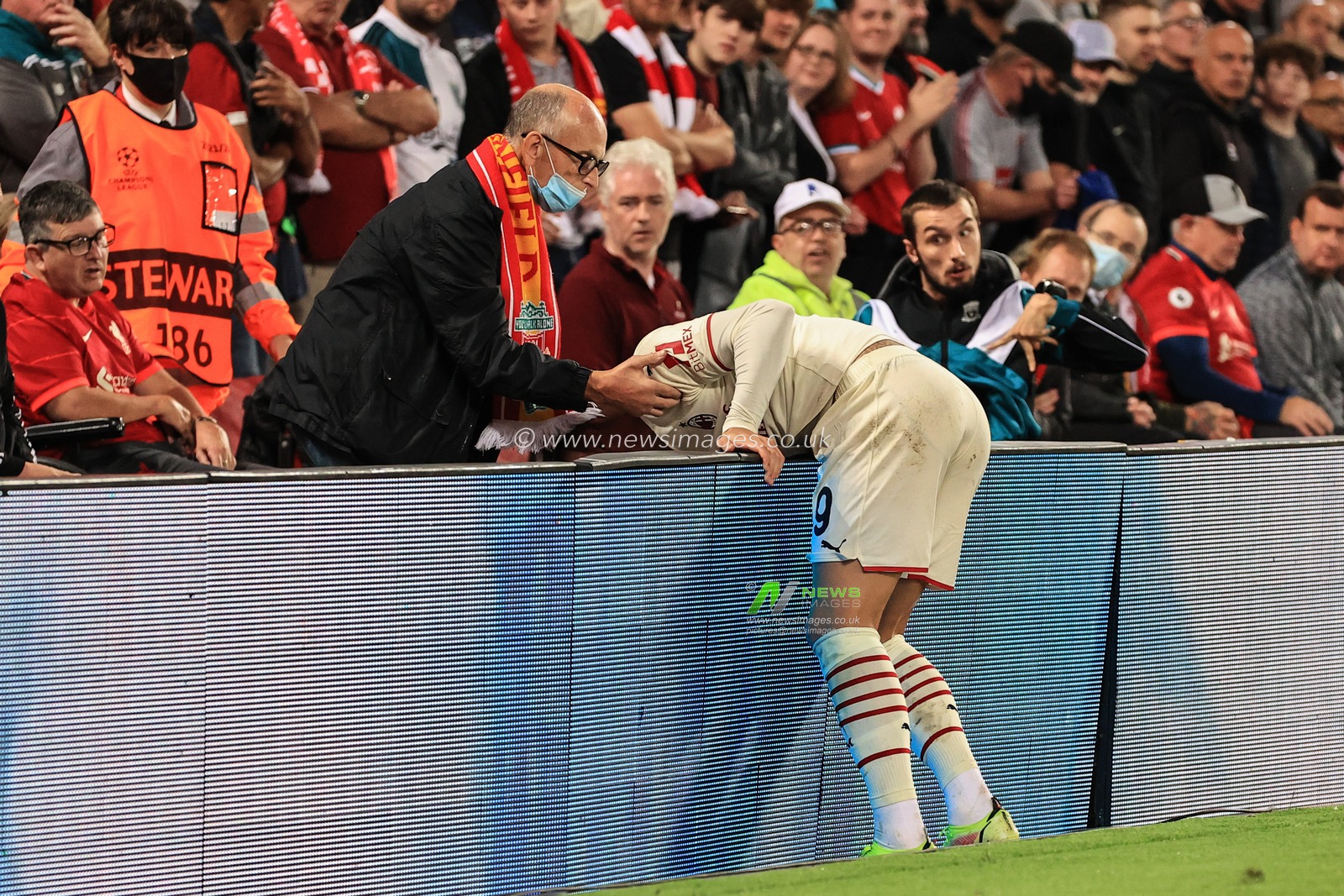 Theo Hernandez #19 of AC Milan ends up over the led boards after over committing and is helped back up by aLiverpool fan