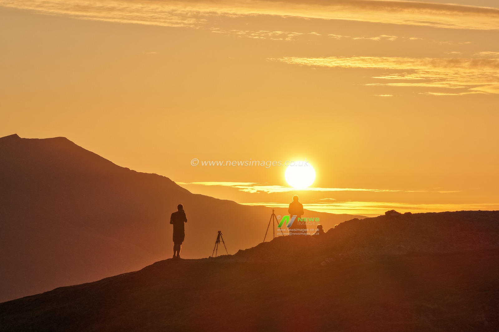 Photographers take pictures as the sun rises from the summit of Catbells overlooking Derwent Water and the town of Keswick In the Lake District, Cumbria, United Kingdom, 19th June 2025.

(Photo by Mark Cosgrove/News Images)
