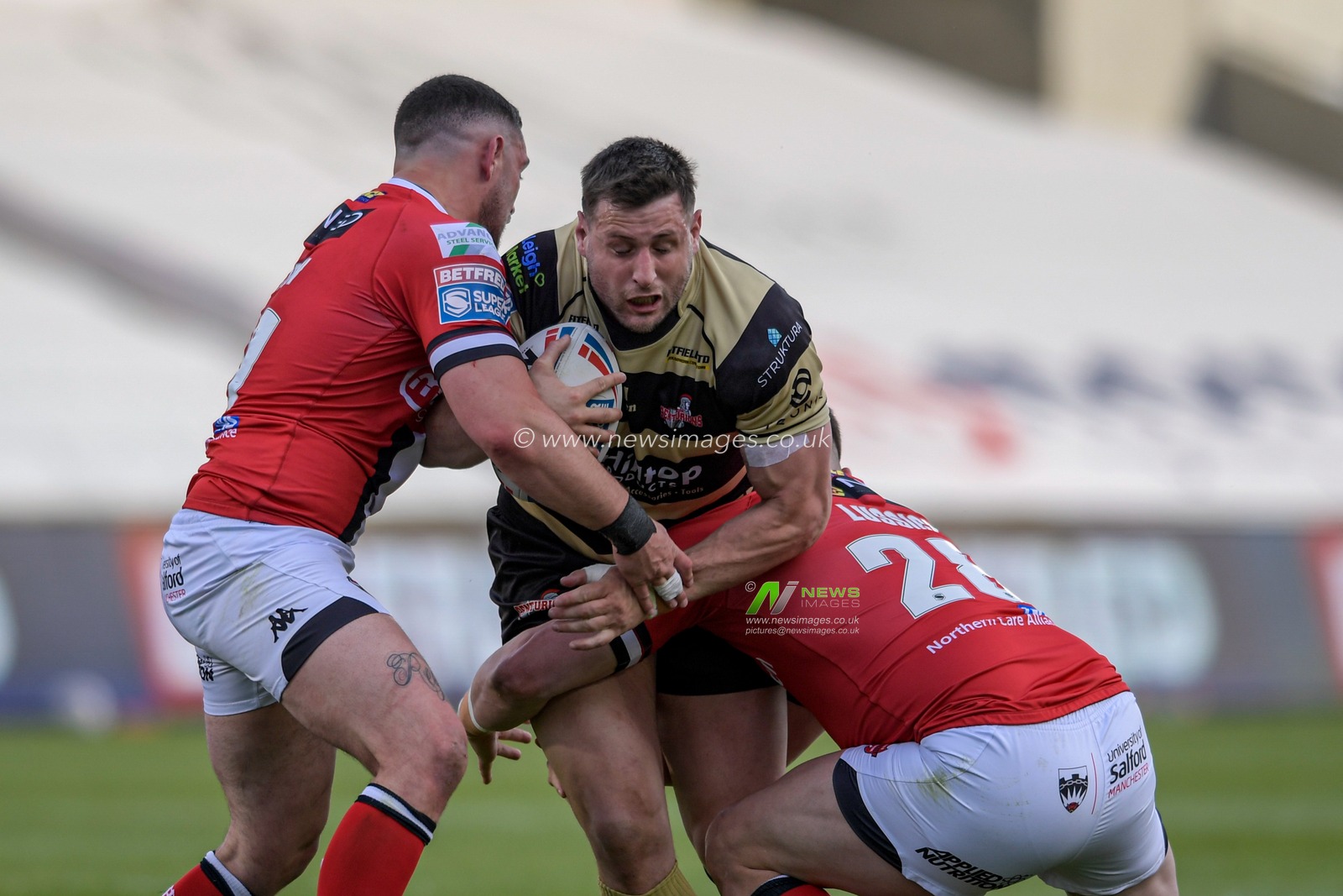 Alex Gerrard (16) of Leigh Centurions is tackled by Darcy Lussick (28) of Salford Red Devils and Declan Patton (29) of Salford Red Devils