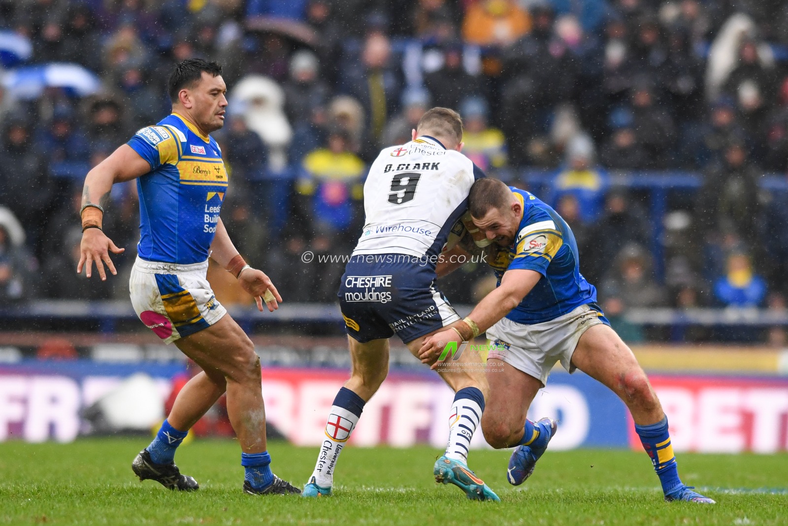 Daryl Clark #9 of Warrington Wolves is tackled by Zane Tetevano #13 of Leeds Rhinos and Cameron Smith #17 of Leeds Rhinos