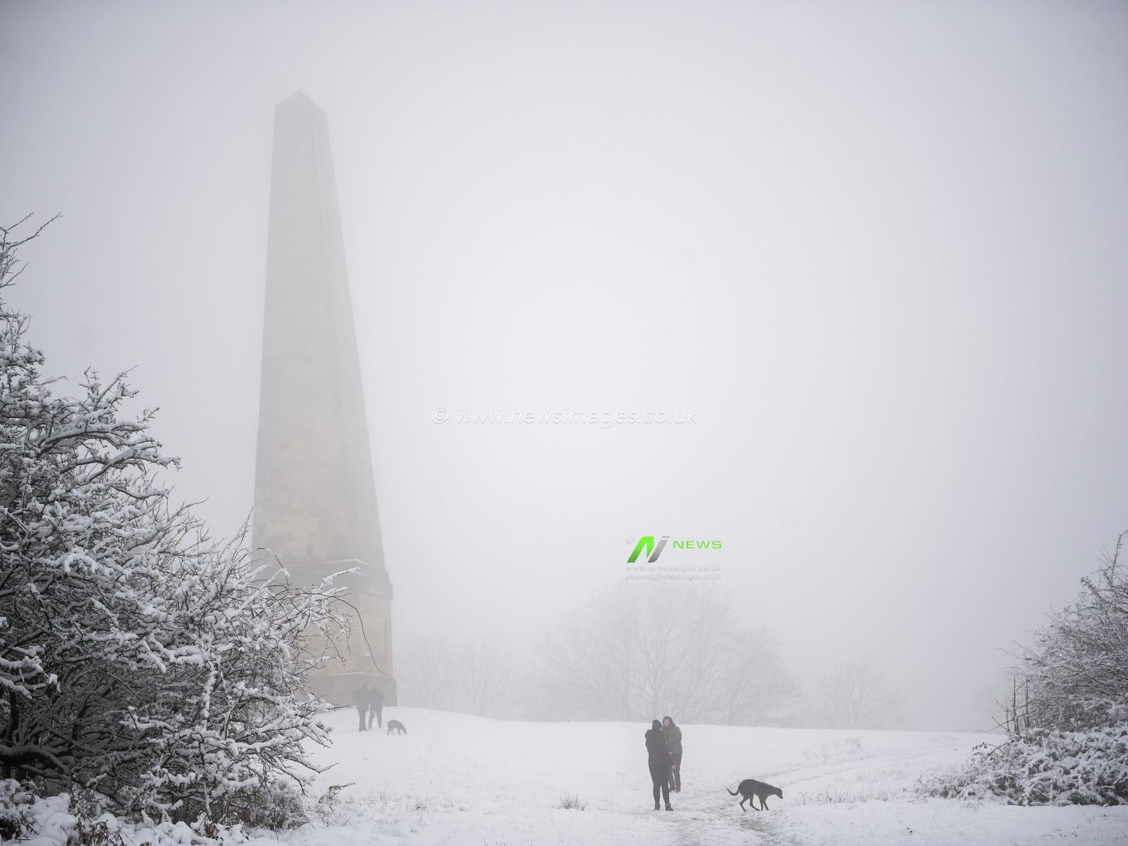 The Eastnor Obelisk hidden in a snow storm with dog walkers talking.