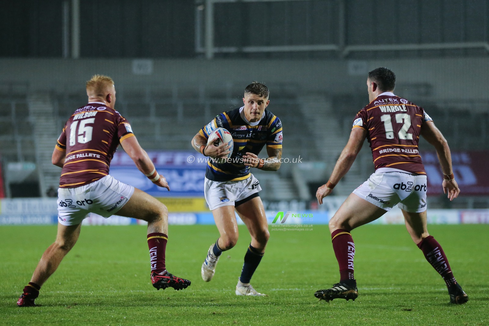 Liam Sutcliffe (15) of Leeds Rhinos on the attack against Oliver Wilson (15) and Joe Wardle (12) of Huddersfield Giants,