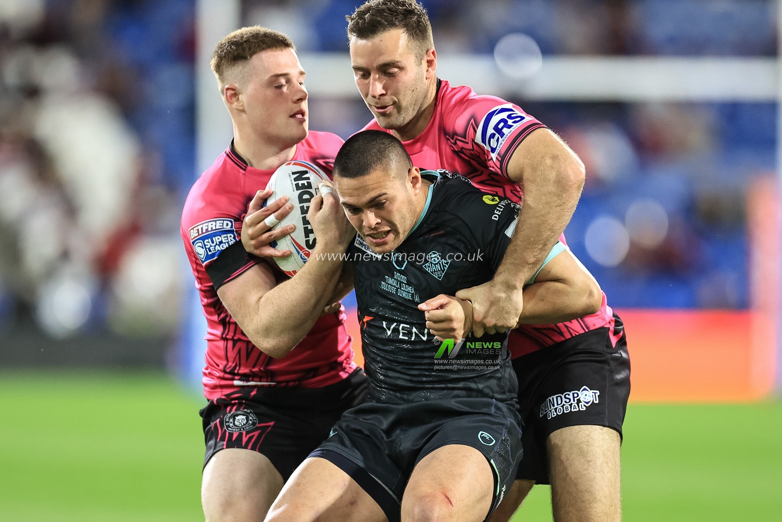 Tui Lolohea #6 of Huddersfield Giants is tackled by Iain Thornley #4 of Wigan Warriors and  Sam Halsall #25 of Wigan Warriors