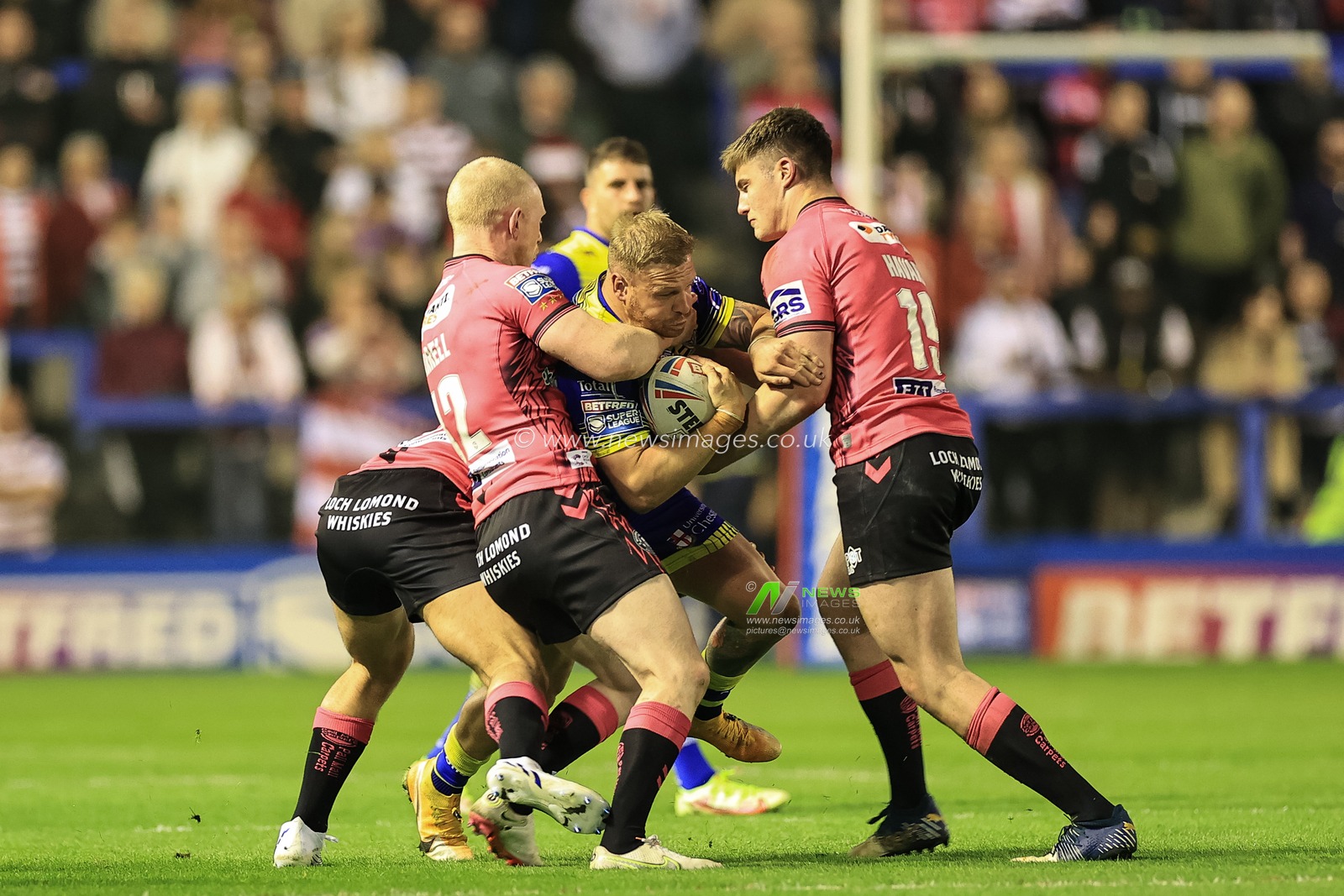 Oliver Holmes #12 of Warrington Wolves is tackled by Liam Farrell #12 of Wigan Warriors and Ethan Havard #19 of Wigan Warriors