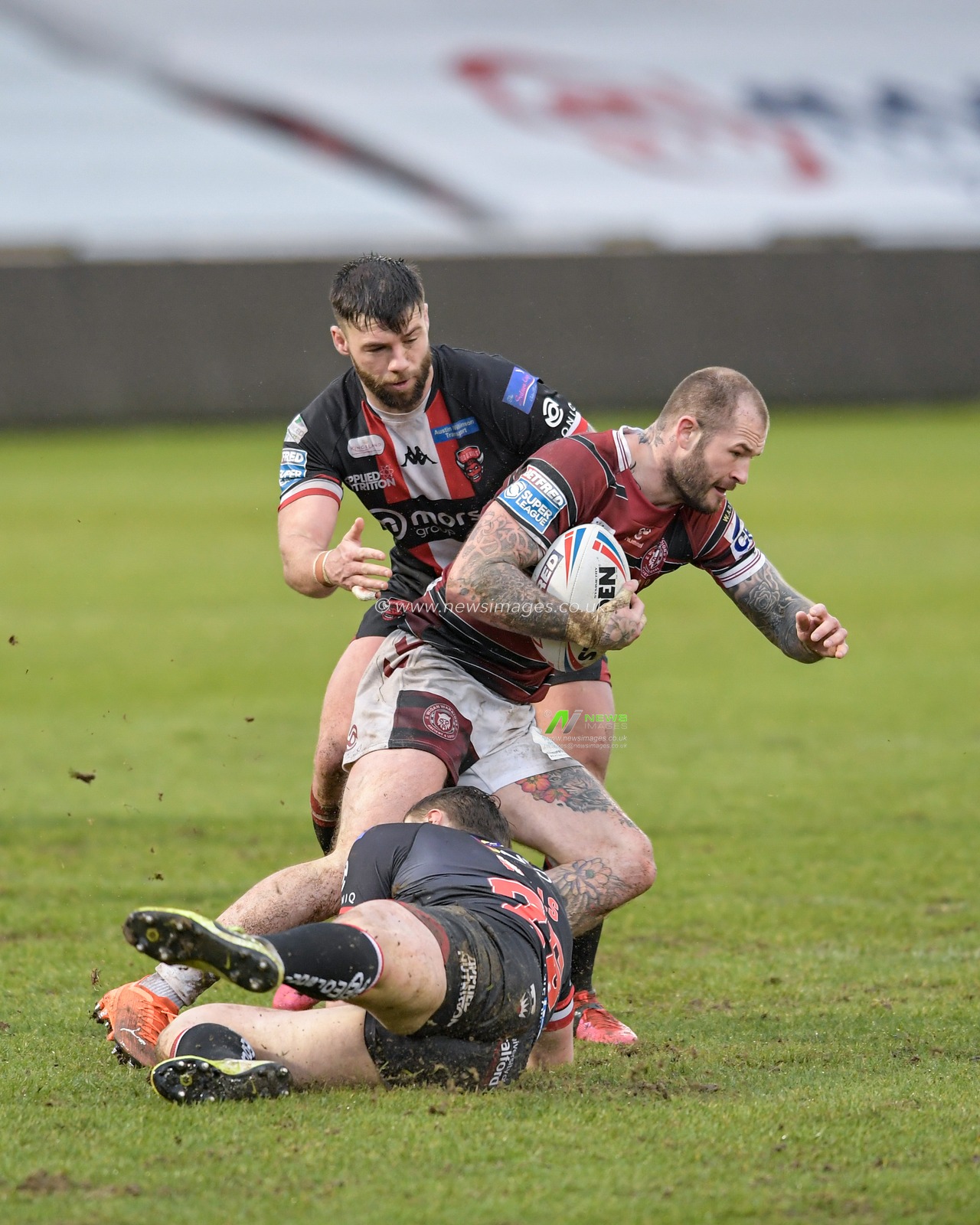 Zak Hardaker (3) of Wigan Warriors is tackled by Jack Wells (26) and Andy Ackers (9) of Salford Red Devils