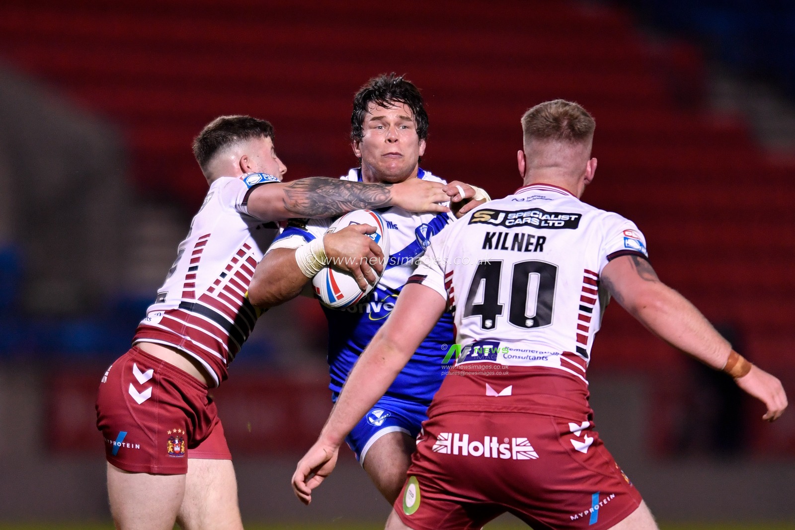 Louie McCarthy-Scarsbrook (13) of St Helens is tackled by Ben Kilner (40) and Amir Bourouh (32) of Wigan Warriors