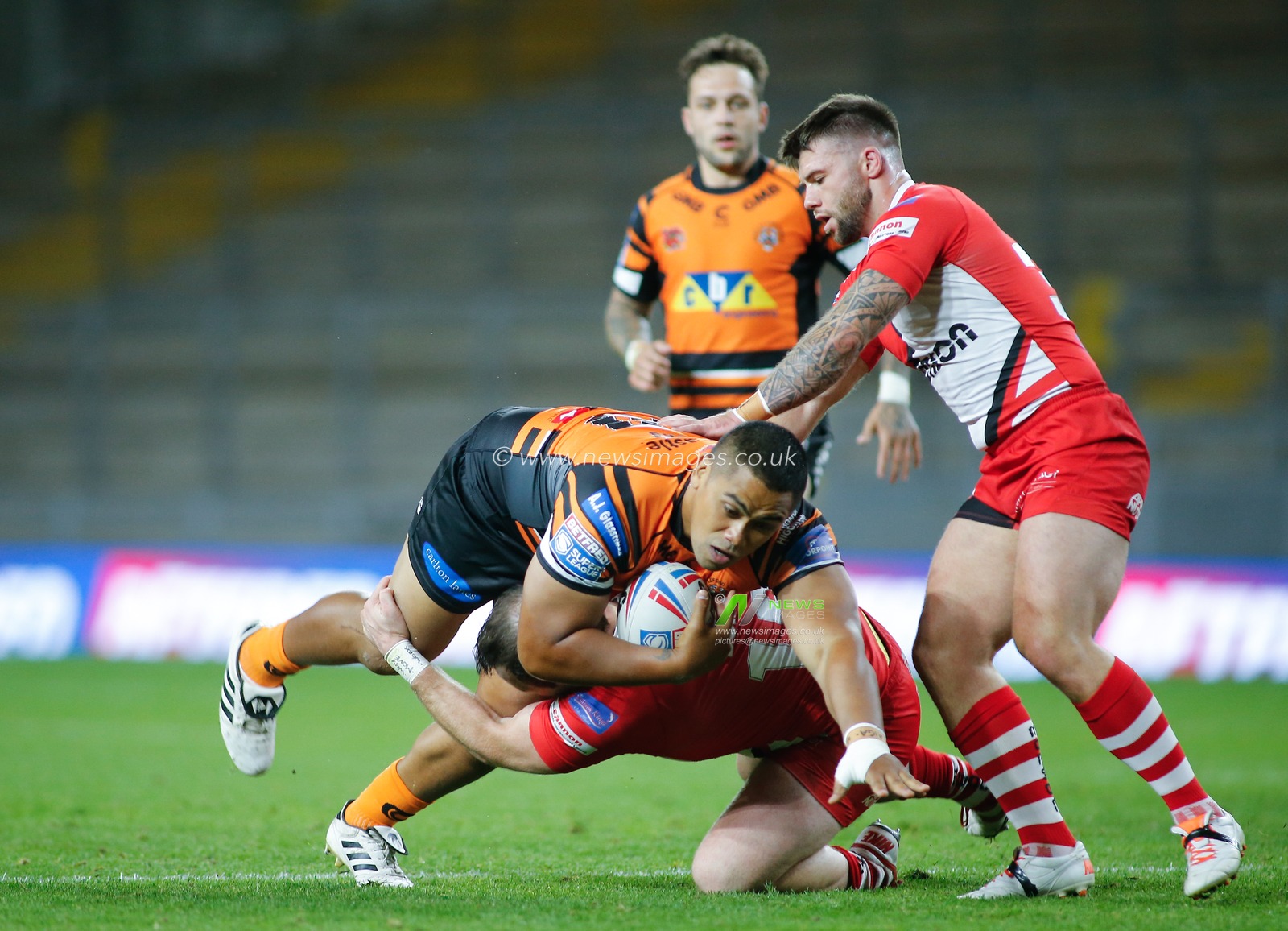 Junior Moors (20) of Castleford Tigers tackled by Greg Burke (16) and Andy Ackers (30) of Salford Red Devils.